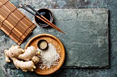 Raw white rice, ginger, soy sauce and sushi chopsticks on gray stone slate background
