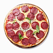 Pepperoni-Pizza mit Basilikum vor weißem Hintergrund (Aufsicht)