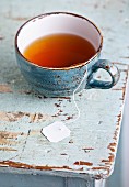 Tasse Tee mit Teebeutel auf hellblauem Holztisch
