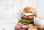 Homemade beef burger with fried egg and vegetables, onion rings and coffee cups on wooden board