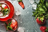 Homemade strawberry lemonade with mint and ice, served with fresh berries over metal tray surface
