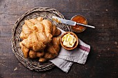 Croissants with butter and jam in wicker tray on dark wooden background