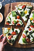 Padron pepper and cherry tomato pizza, gluten-free and whole-grain, a hand taking a slice