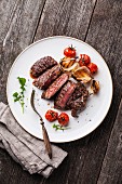 Sliced medium rare grilled Beef steak Ribeye with grilled onions and cherry tomatoes on plate