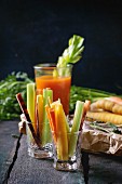 Sliced colorful raw carrots and celery as vegetarian snack and glass cup of fresh orange and carrot juice
