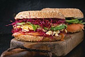 Two Bagels with salted salmon, spinach, beetroot sprouts, avocado and scrambled egg on wooden chopping board