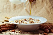 Plate of muesli with pouring milk and honey, cinnamon and nuts over textile background