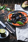 Vintage plate with black homemade ravioli with salted salmon, served with cutlery on wooden table