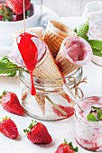 Wafer cones with strawberry ice cream with pouring syrup and fresh strawberries
