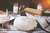 Dough on wooden table with flour, rolling-pin and jars with backing ingredients