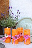 Orangefarbene Kerzen mit Blüten und Geschenkbändern dekoriert