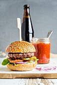 Fresh homemade burger on white wooden serving board with onion rings, salsa sauce and bottle of beer