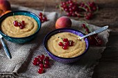 Apricot vanilla millet pudding in two small bowls and topped with red currant