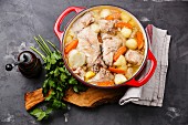 Stewed rabbit with potatoes and carrot in cast iron pot on concrete background