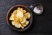 Homemade crispy Potato chips and sea ​​salt on dark wooden background