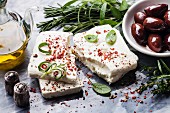 Feta cheese with olives and green herbs on gray marble background