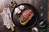 Raw roast beef Rump, seasonings and meat fork on dark wooden background