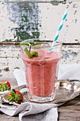 Glass of red strawberry smoothie with chia seeds, served with retro cocktail tube, fresh mint and strawberries