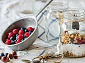 Glass jar with homemade granola and yogurt served with nuts, raspberries and blackberries in vintage colander