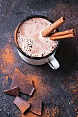 Vintage mug of hot chocolate with cinnamon sticks over dark background
