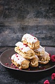 Ceramic plate of mini eclairs with white chocolate, served with dry raspberry on dark background