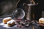 Tea drinking with eclairs and chopped chocolate, served with vintage teapot and cutlery over dark background