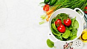 Fresh organic garden vegetables in colander bowl on white rustic stone background