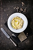 Plate of homemade hummus with vintage knife and raw chick-pea over dark table