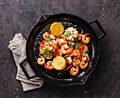Prawns roasted on frying grill pan with lemon and garlic on dark background