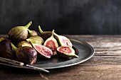 Whole and sliced figs on a metal plate with knife on a wooden table