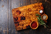 Chopping cutting kitchen board, salt, pepper and rosemary on dark wooden background