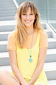 Blonde Frau in orangefarbenem T-Shirt unter gelbem Sommerkleid sitzt auf einer Treppe