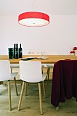 Rote Leuchte über einem schlichten Holztisch mit modernen Stühlen