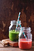Glass jar with green spinach and red strawberry smoothie over wooden table