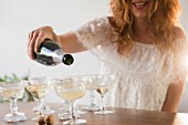 Lächelnde Frau giesst Champagner in Sektschalen