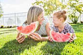 A mother and daughter lying on the grass eating watermelon