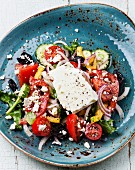 Greek salad with feta cheese and sun-dried olives on blue background