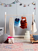 Wooden clothes rack with children's costumes in front of gray wooden paneling and pompom chain