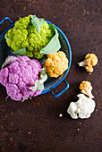 Various brightly coloured cauliflower florets in an enamel colander
