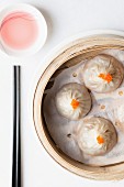 Steamed Chinese dumplings with fish roe in bamboo steaming basket with chopsticks and dipping sauce