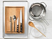 Various kitchen utensils: pot, strainer, glass bowl, vegetable peeler, spoon