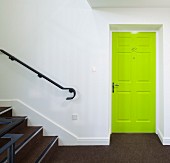 Neongrüne Kassettentür in weißem Treppenhaus mit braunem Teppichboden