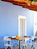 Esstisch und weiße Stühle vor blauer Wand auf mediterraner Terrasse