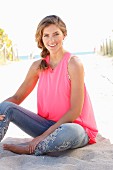 A young woman wearing a pink top and jeans with flower embroidery on the beach