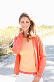 Blonde Frau in orangefarbenem T-Shirt, Cardigan und weißer Hose am Strand