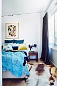 Blaue, gestrickte Tagesdecke auf Doppelbett und Tierfellvorleger im Schlafzimmer