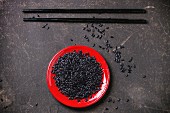 Uncooked black rice on red plate with black wooden chopsticks over black surface
