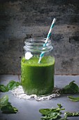Glass jar with green smoothie, served with baby spinach leaves over metal table