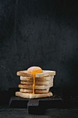Pile of toasts bread with flowing sugared yolk on black wooden cutting board over black textured background