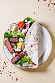 Overhead view on plate with taco with feta cheese and beef over white wooden background